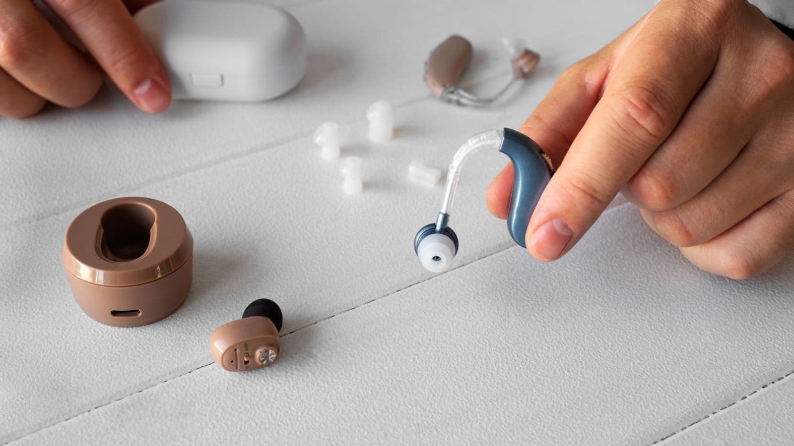 A person holds a hearing aid in one hand and a small device in the other, demonstrating assistive technology for hearing.
