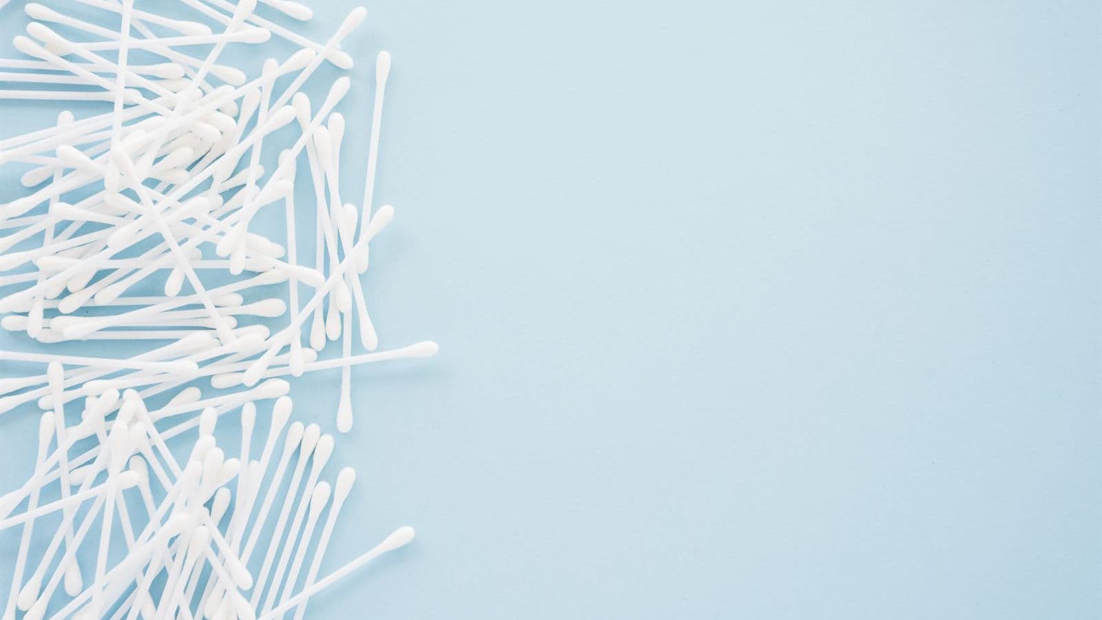 White cotton swabs piled on a blue background, not recommended for cleaning inside the ears.