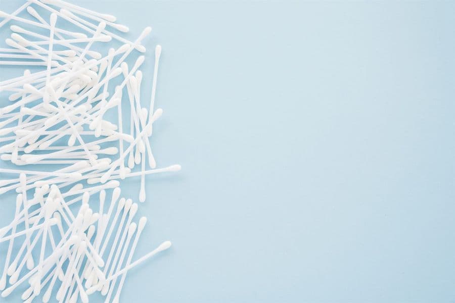 White cotton swabs piled on a blue background, not recommended for cleaning inside the ears.
