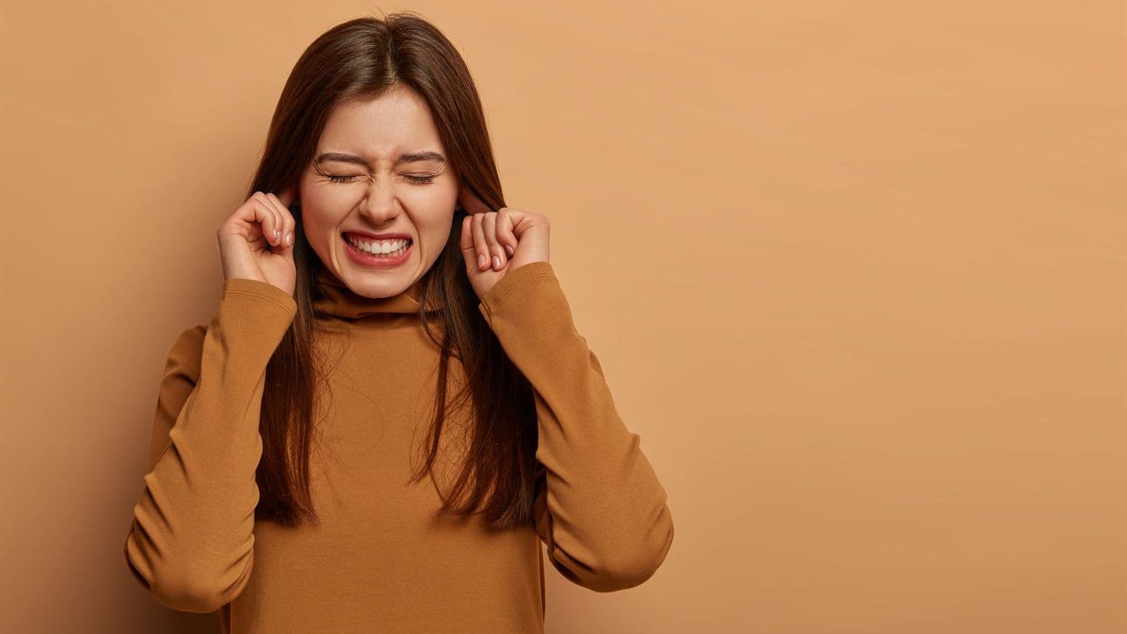 Woman covering her ears in discomfort from ringing, a common sign of tinnitus