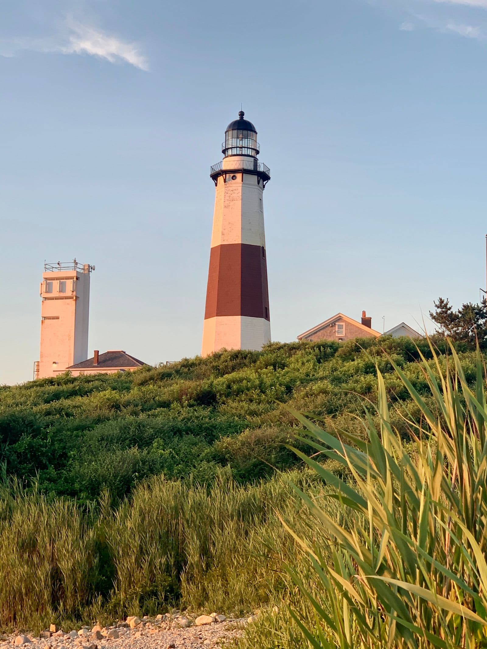 Montauk Point Lighthouse surrounded by greenery under a summer sky