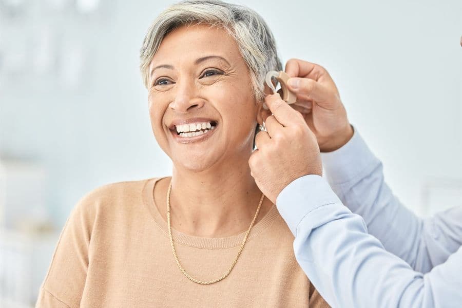 An audiologist fitting a behind-the-ear hearing aid on a smiling older woman