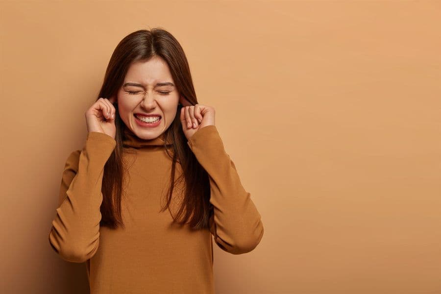 Woman covering her ears in discomfort from ringing, a common sign of tinnitus